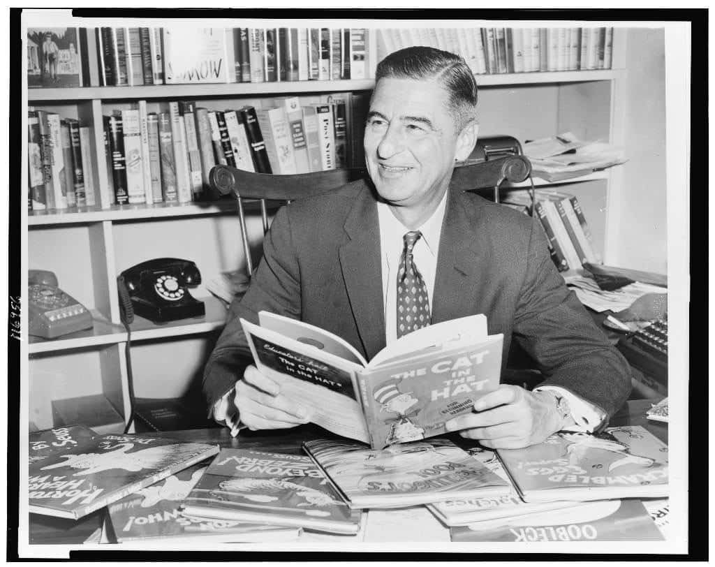 ted-geisel-dr-seuss-half-length-portrait-seated-at-desk-covered-with-his-bo-1544042348839.jpg