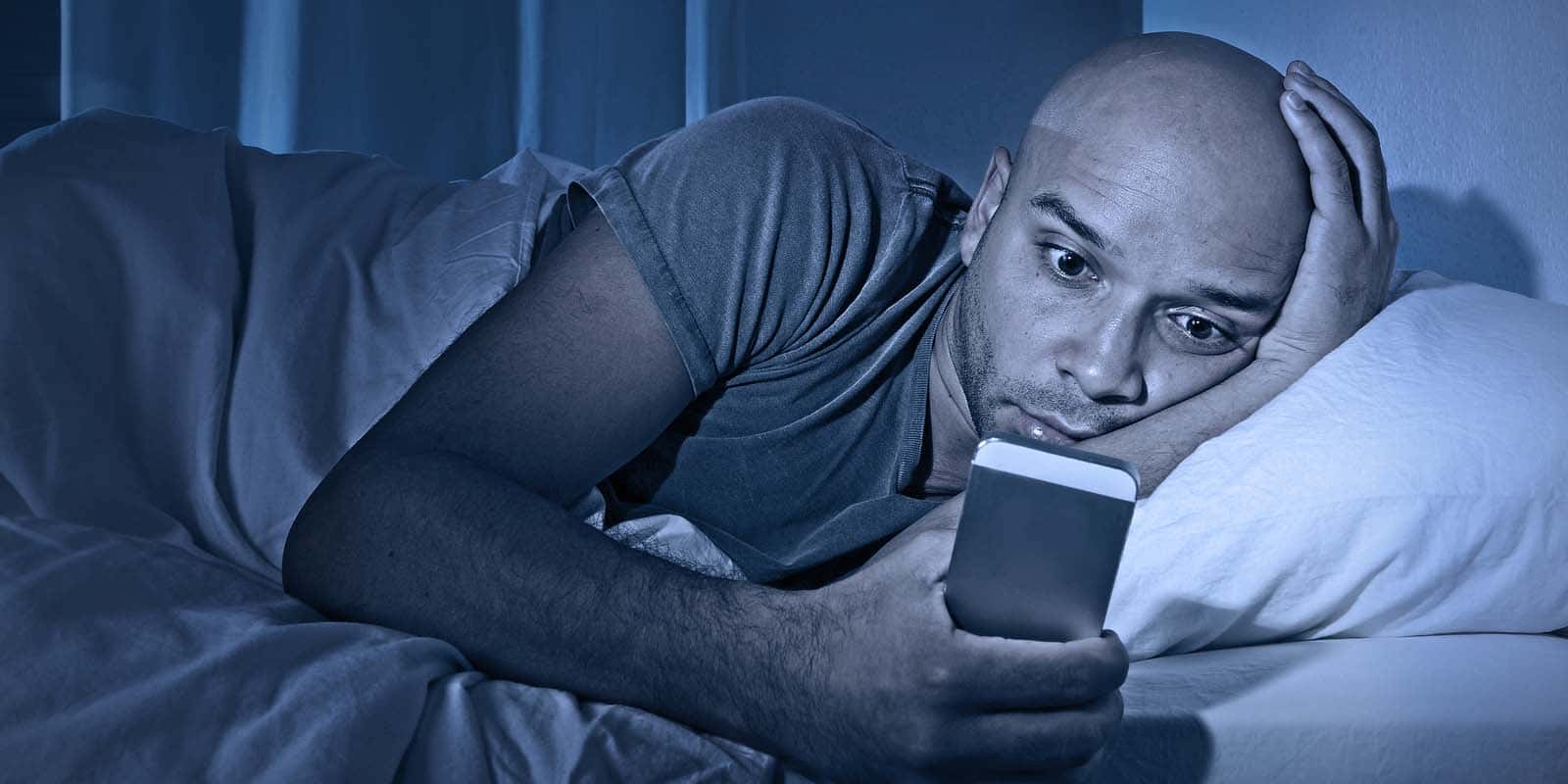 Young Cell Phone Addict Man Awake At Night In Bed Using Smartpho