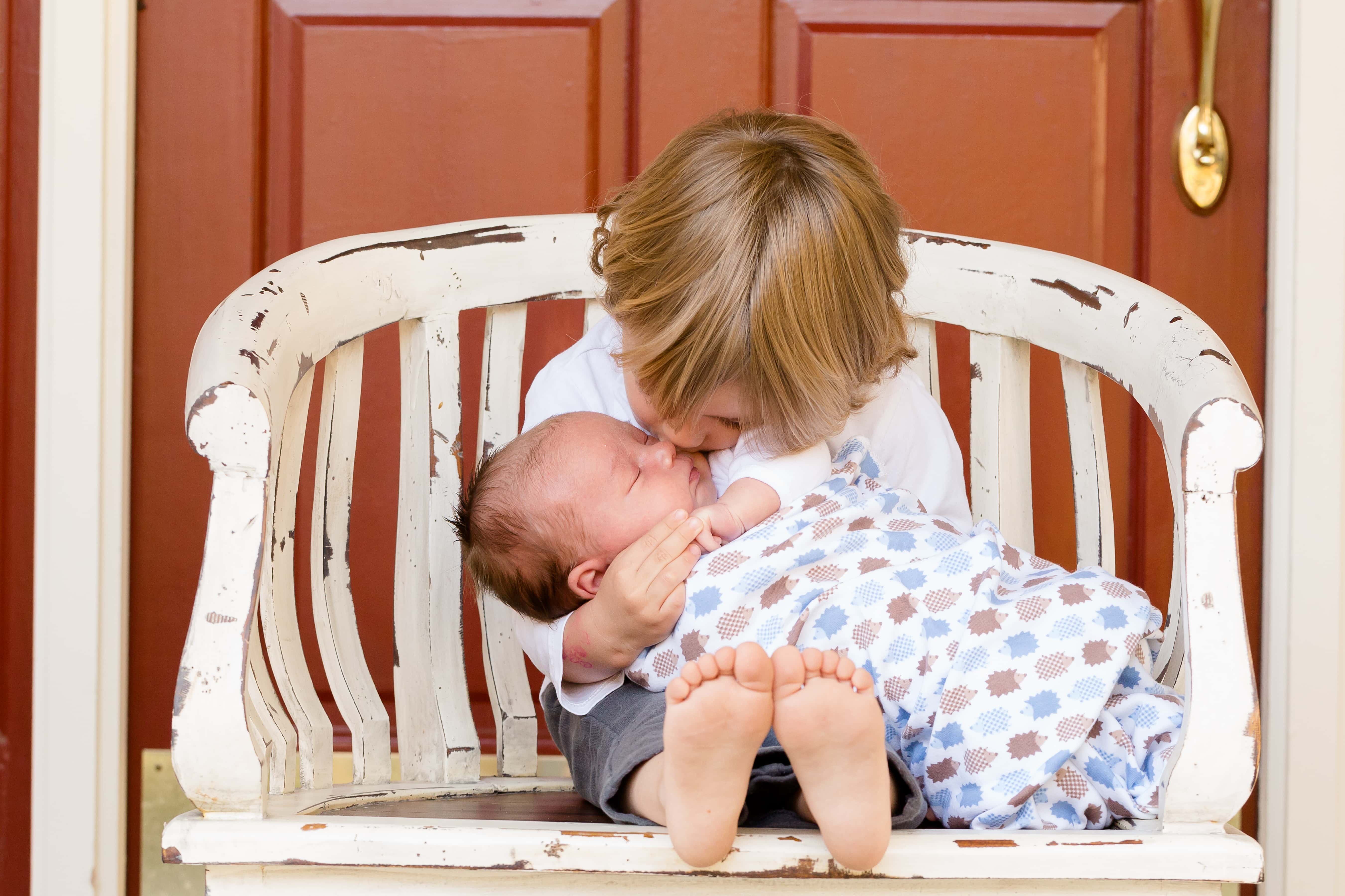 Canva - Boy Carrying and Kissing Baby Sitting on Chair