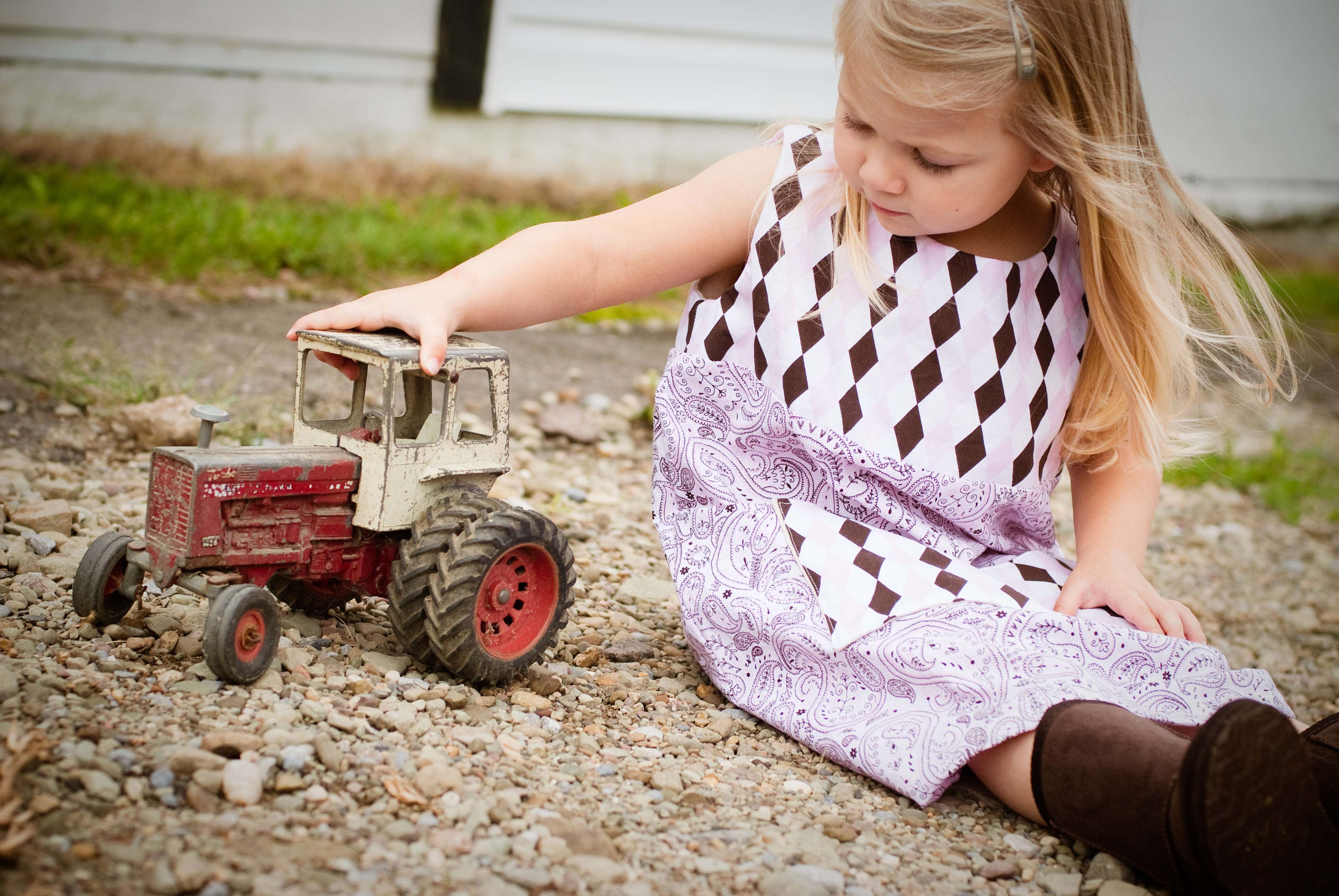 Canva - Girl Sitting on Brown Sand While Playing Tractor Toy