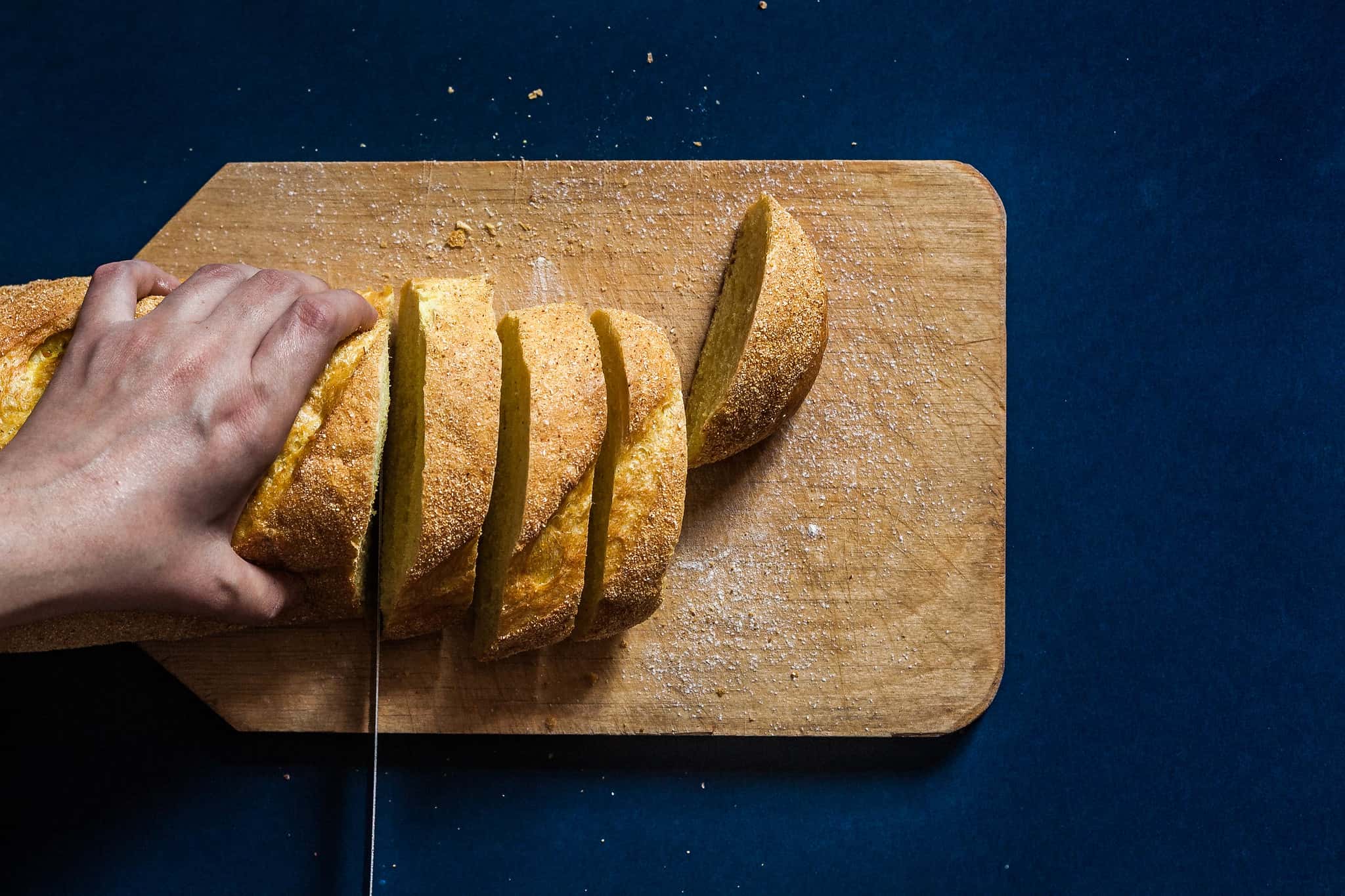 Top view to a woman's hand cutting bread on dark blue background