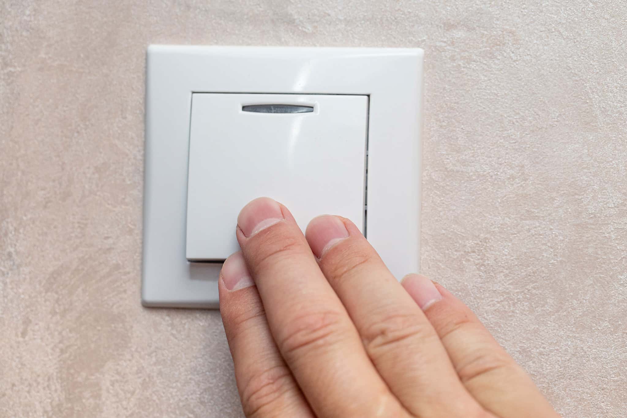 Man's hand with fingers on light switch, about to turn off the lights