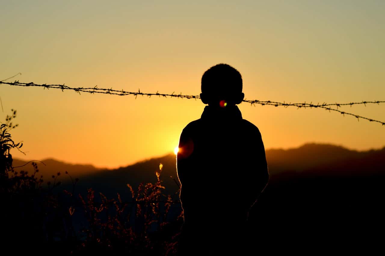 silhouette-of-boy-standing-near-barbed-wire-fence-during-735010