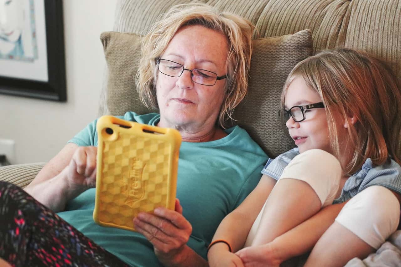 woman-holding-tablet-lying-beside-girl-wear-eyeglasses-1310121