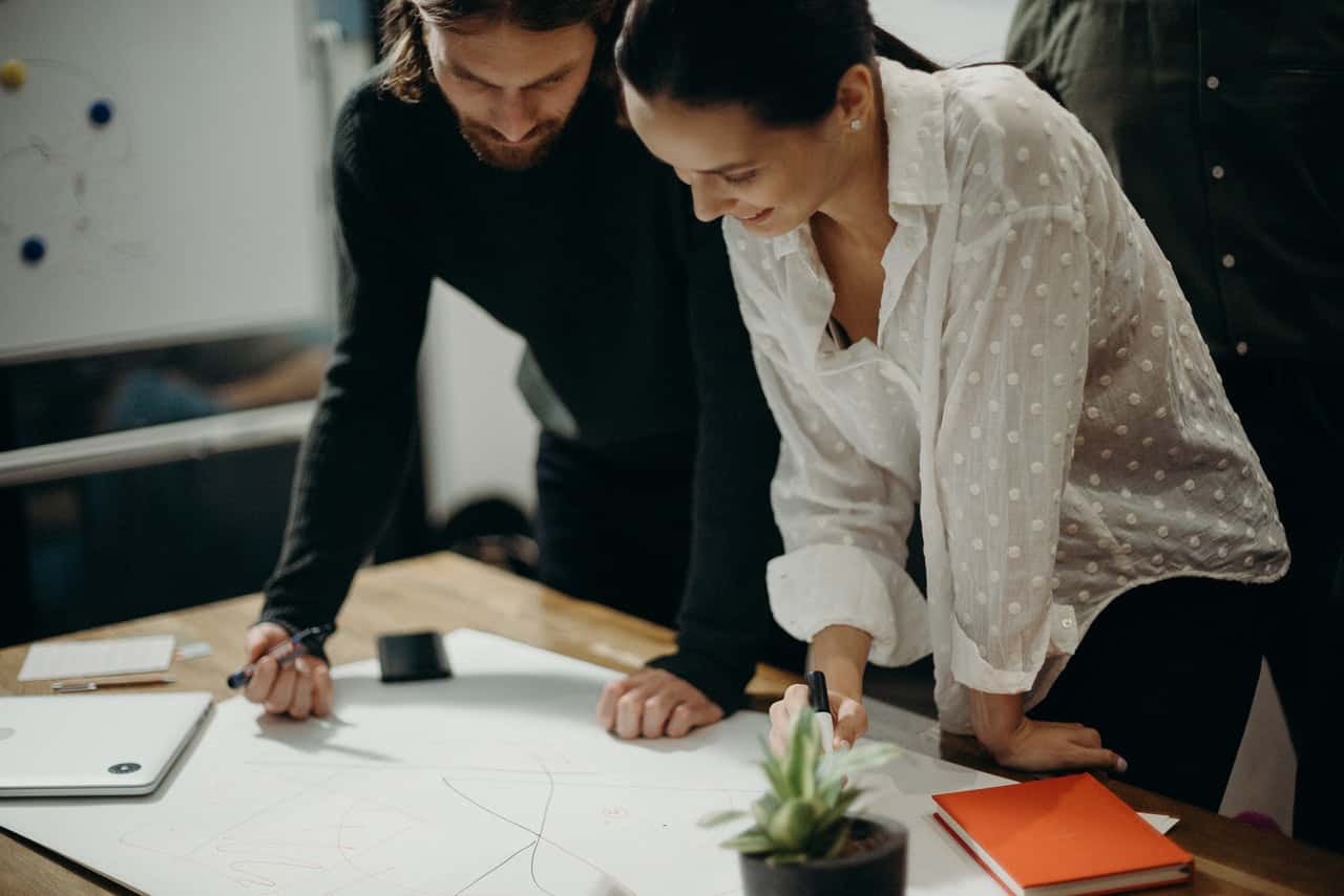 man-and-woman-leaning-on-table-staring-at-white-board-on-top-3205570