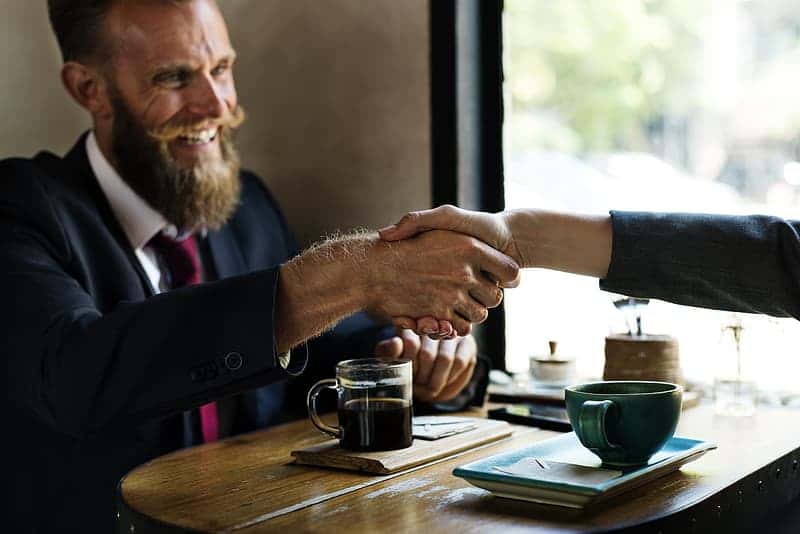 man-in-black-suit-in-front-of-coffee-on-table-shaking-hands-on-person-in-other-side