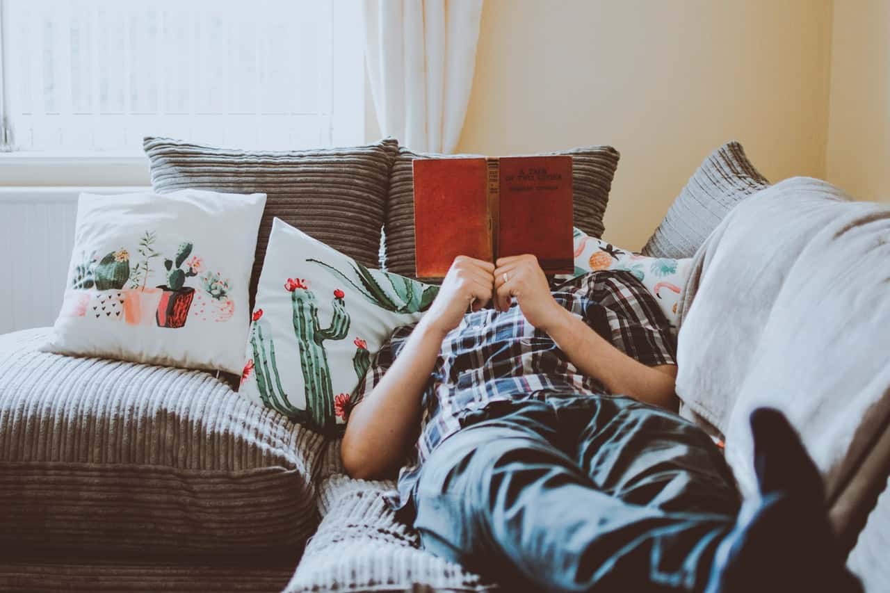 person-laying-on-sofa-while-reading-book-1471991