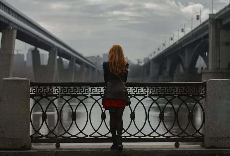woman-wearing-black-jacket-standing-beside-black-metal-rails-watching-concrete-bridge