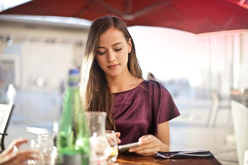 a-young-blonde-woman-wearing-a-purple-red-dress-looking-at-her-mobile-phone-screen-at-a-restaurant