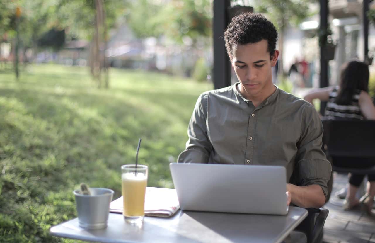 focused-black-male-freelancer-using-laptop-in-street-cafe-3799115