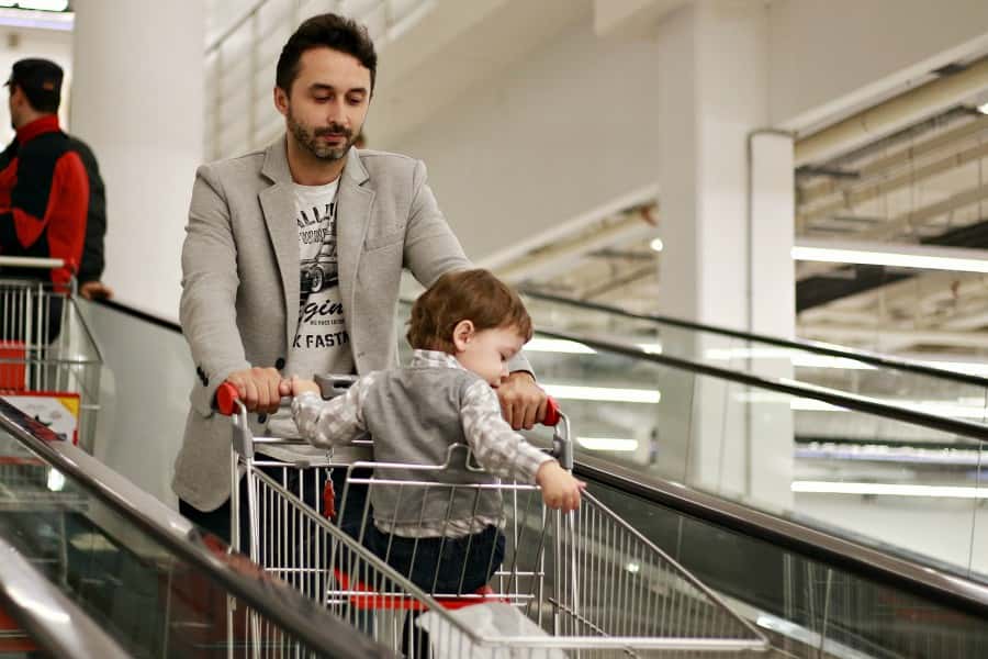 man-pushing-shoppers-cart-with-baby-sitting-inside-1621140