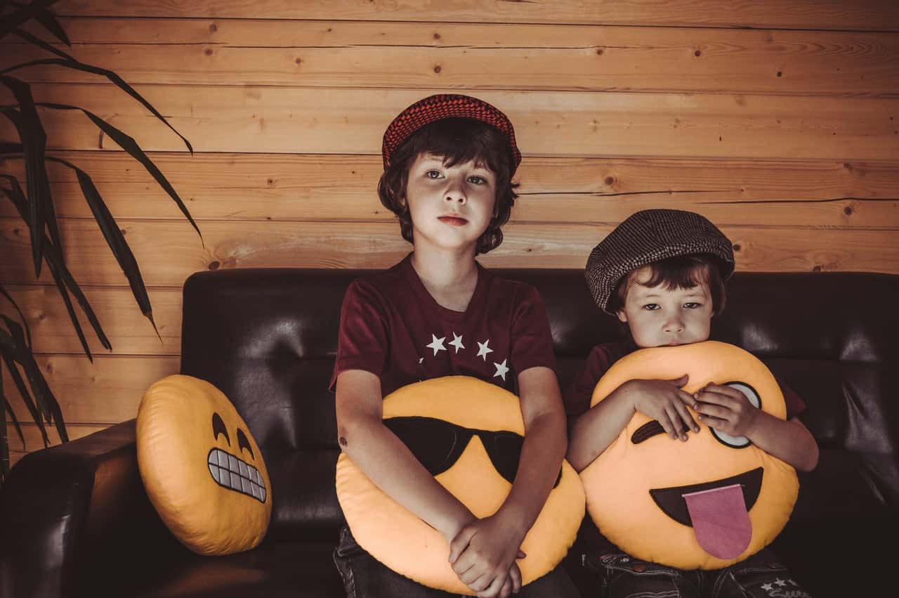 two-boys-sitting-on-sofa-holding-emoji-throw-pillows-1564896