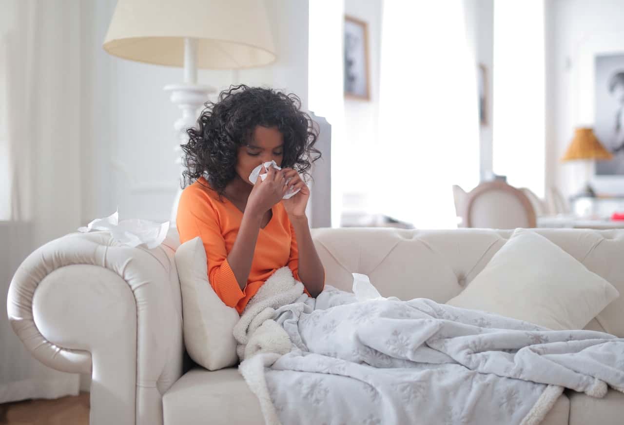 young-black-woman-covered-with-blanket-blowing-nose-3960031