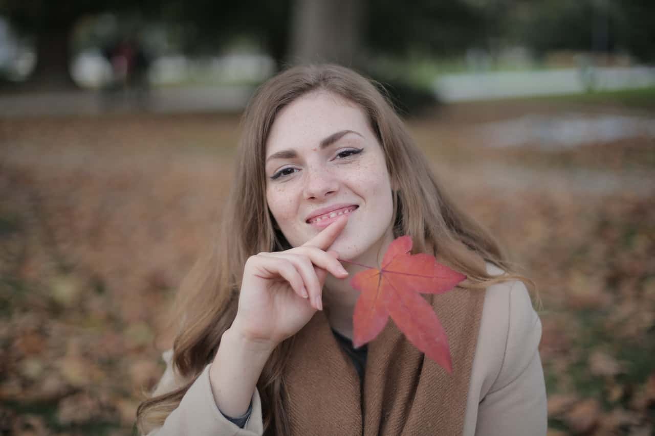 happy-adult-woman-with-red-leaf-in-city-park-in-autumn-3776554