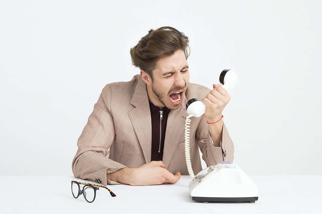 man-wearing-brown-suit-jacket-mocking-on-white-telephone-1587014