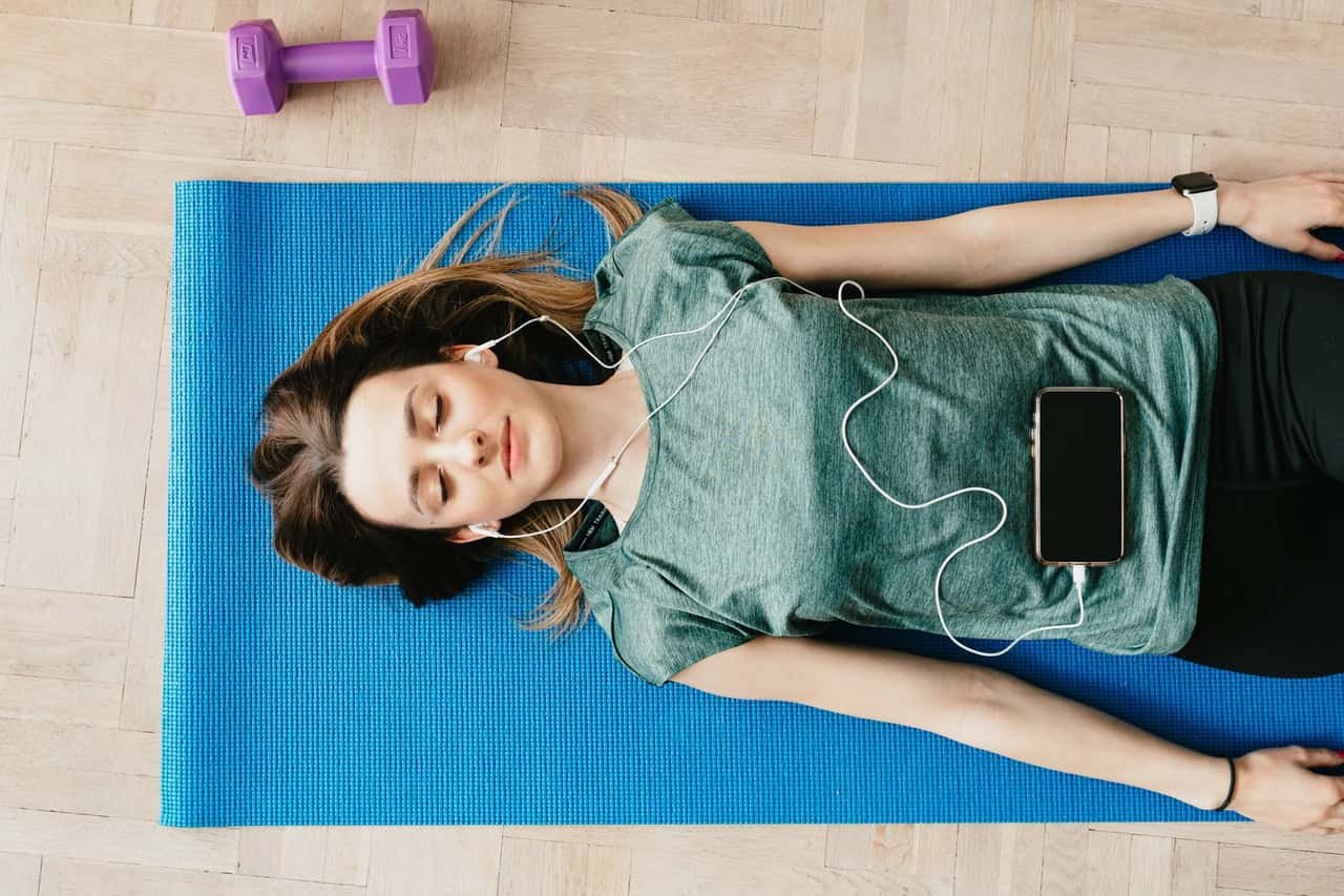 peaceful-woman-in-earphones-resting-in-shavasana-pose-at-4498217