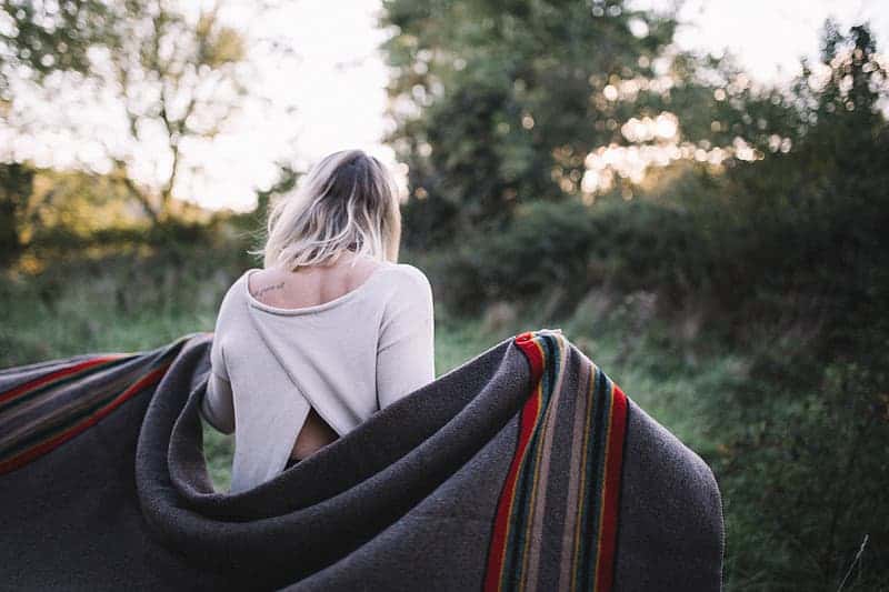 woman-wearing-white-long-sleeved-top-holding-gray-blanket-surrounded-by-trees
