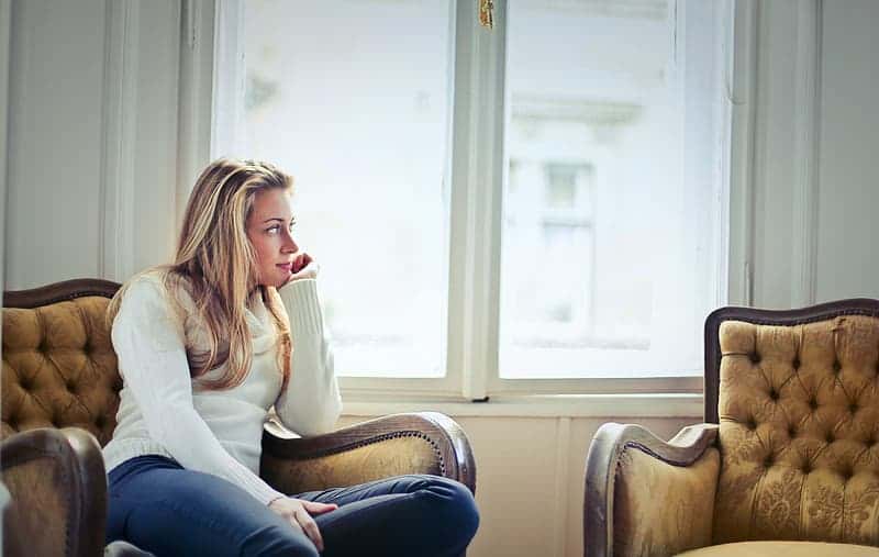 young-woman-supporting-her-chin-by-hand-while-sitting-on-chair-near-window