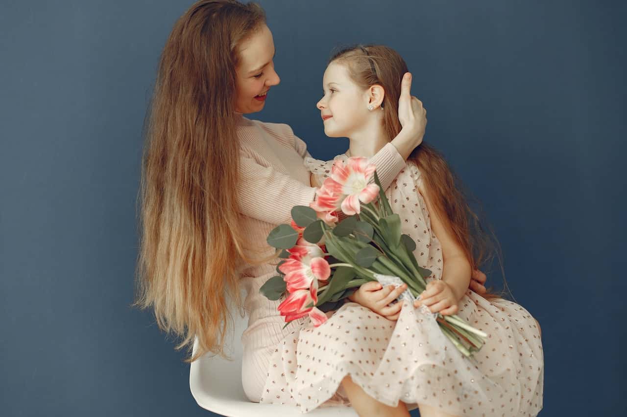cheerful-woman-hugging-little-daughter-with-flowers-3875347