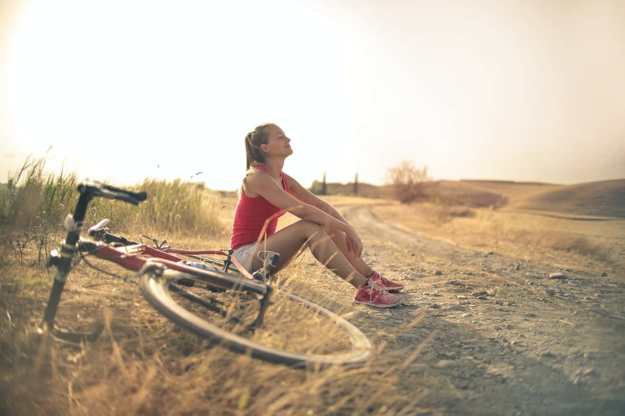 sportive-woman-with-bicycle-resting-on-countryside-road-in-3771836