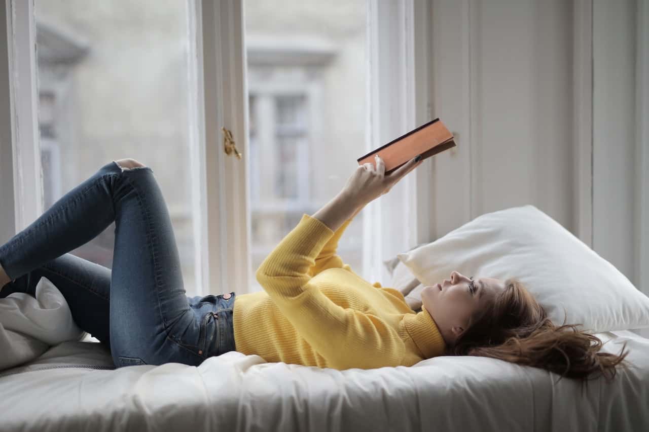 woman-in-yellow-sweater-lying-on-bed-while-reading-book-3786796
