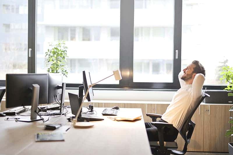 young-man-in-white-shirt-sitting-on-black-rolling-chair-with-hands-behind-head