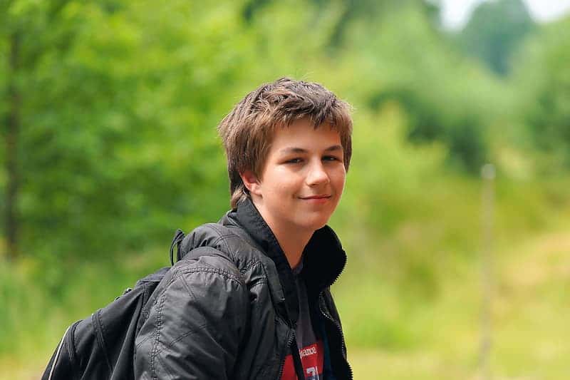 boy-wearing-black-jacket-and-backpack-standing-near-plant