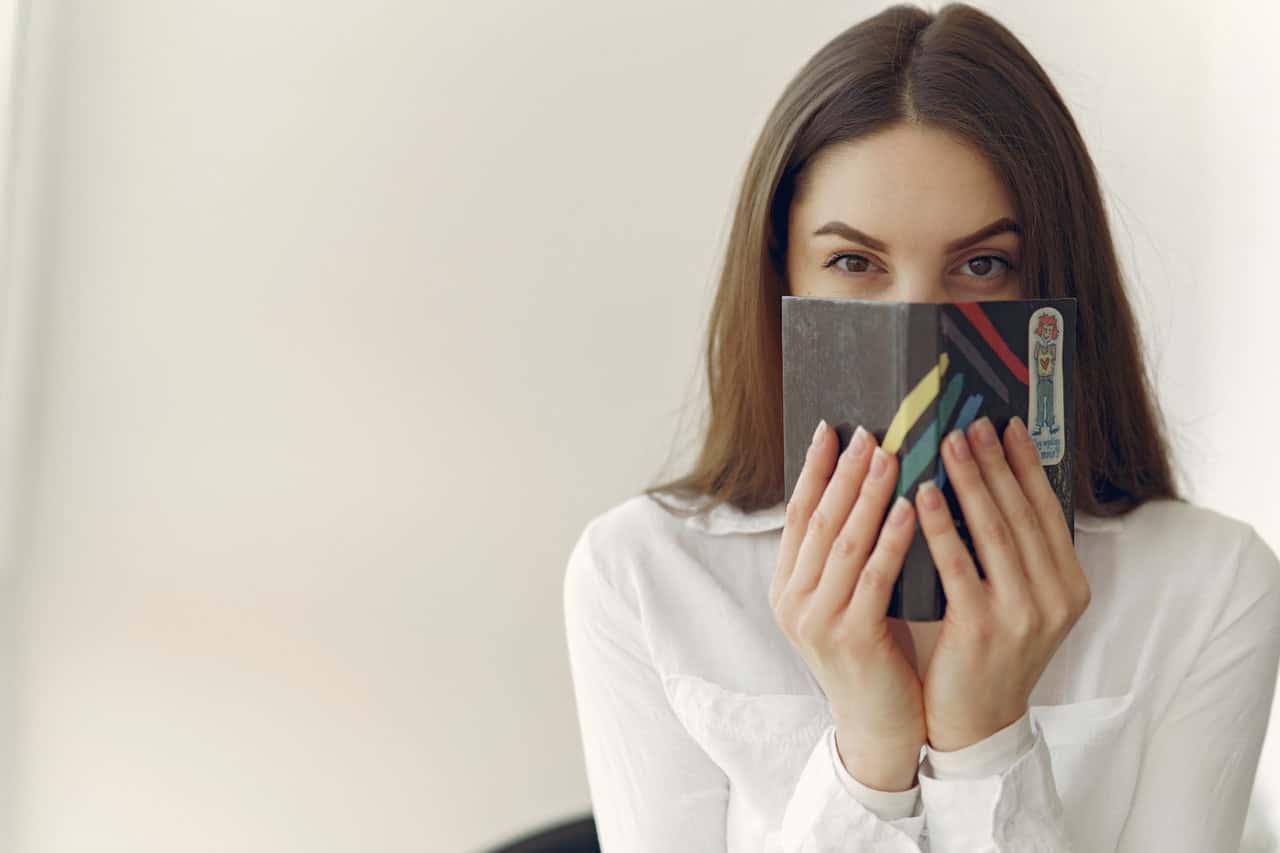 charming-woman-covering-face-with-notebook-in-office-4149079
