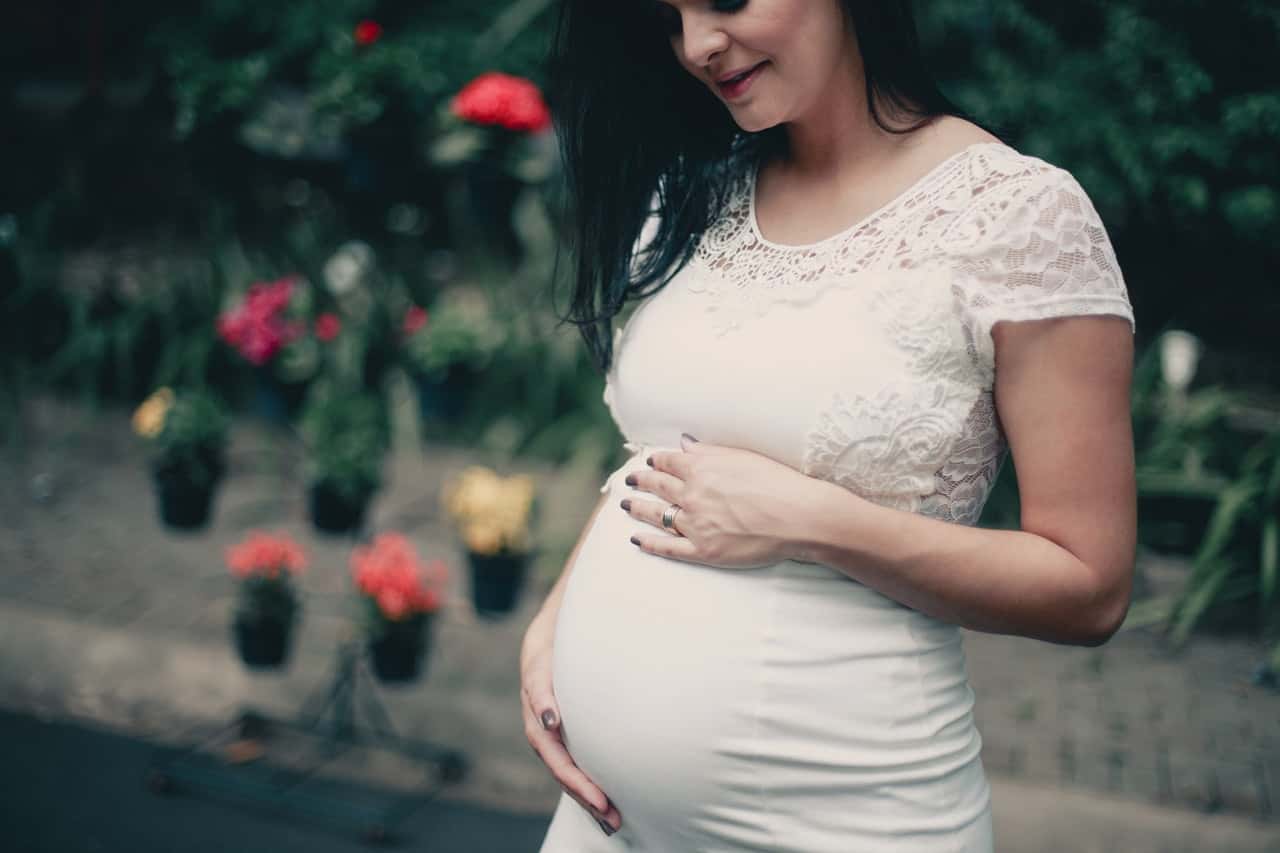 close-up-photo-of-pregnant-woman-in-white-dress-holding-her-2100341