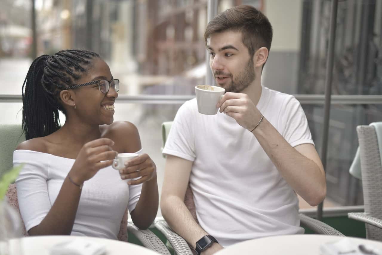 happy-diverse-couple-drinking-coffee-in-cafeteria-in-3978139