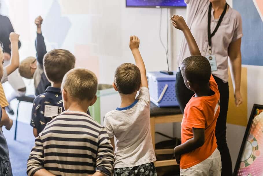 teacher-teaching-children-raising-hands-in-classroom