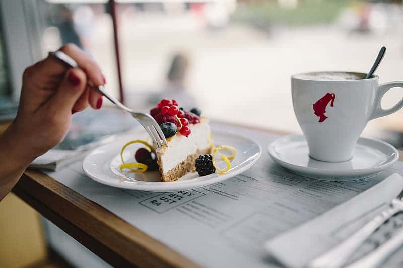 woman-enjoying-cheese-cake-and-a-coffee-with-fruits-in-a-cafeteria