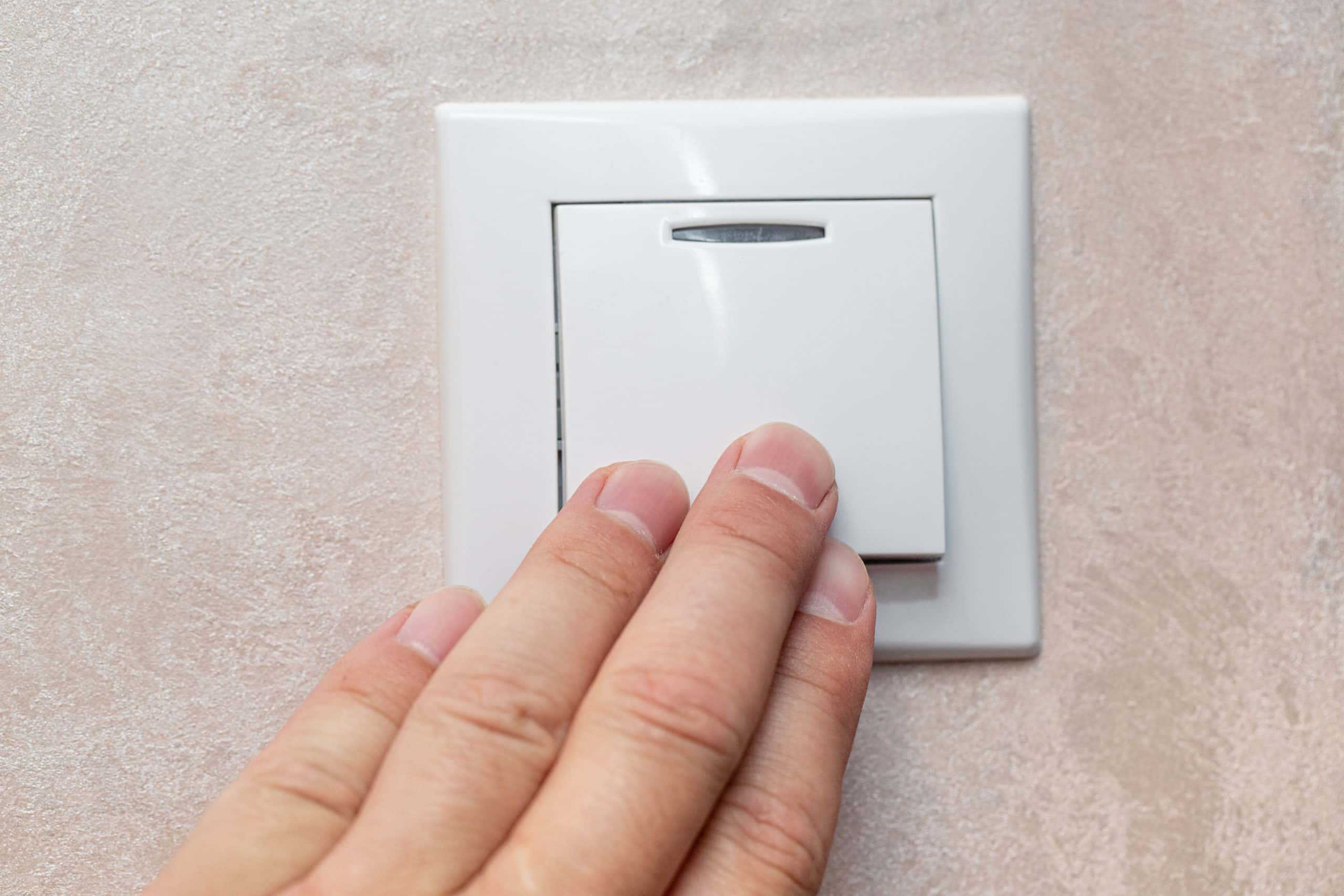 Man's hand with fingers on light switch, about to turn off the lights