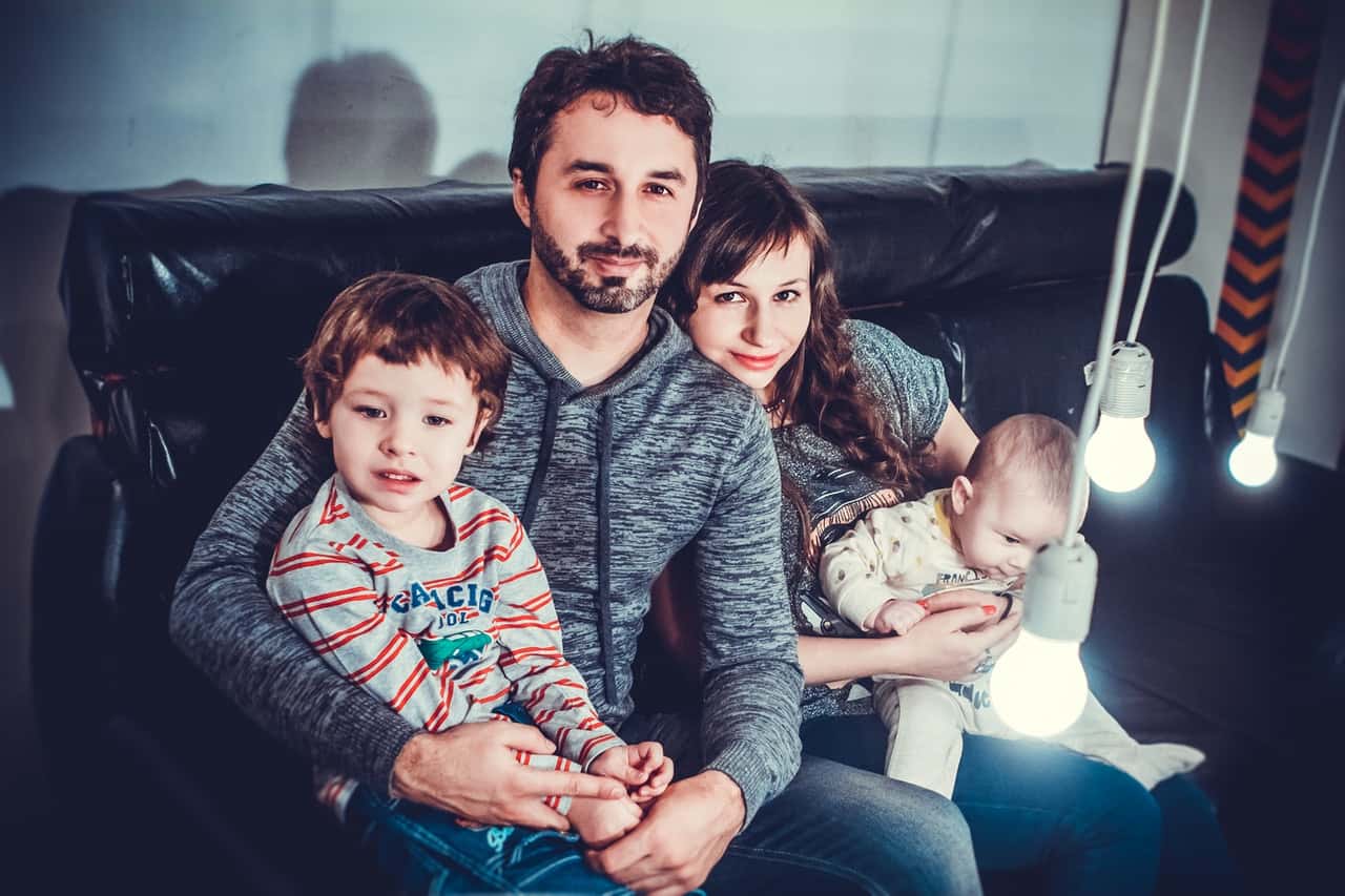 man-and-woman-carrying-babies-while-sitting-on-chair-1648396