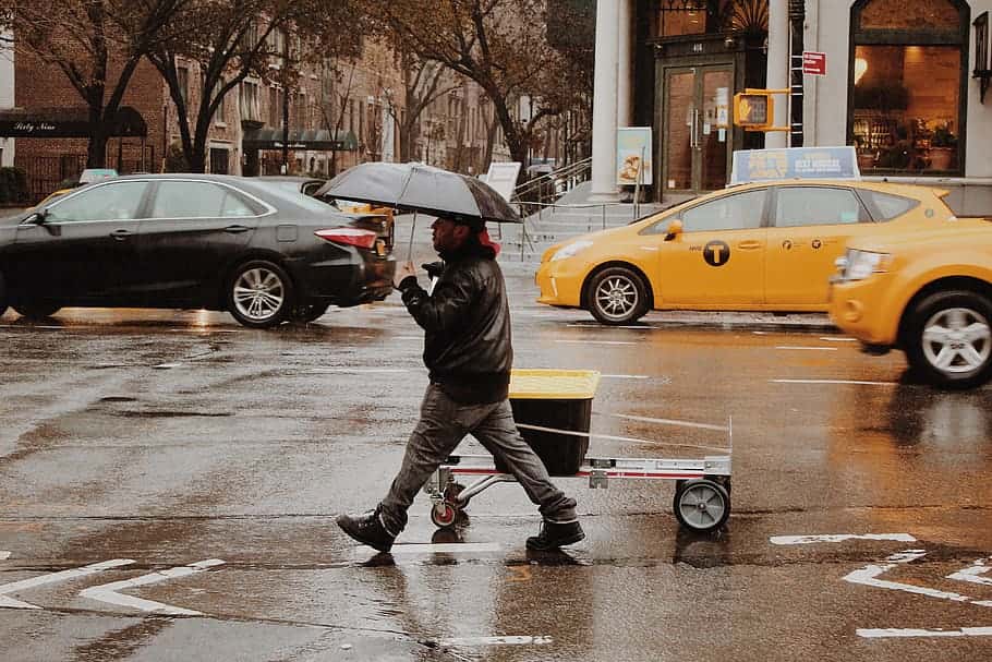 man-using-umbrella-walking-along-wet-road