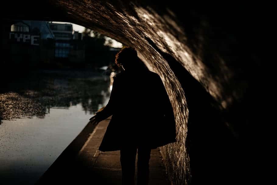 person-wearing-black-coat-walking-under-the-bridge