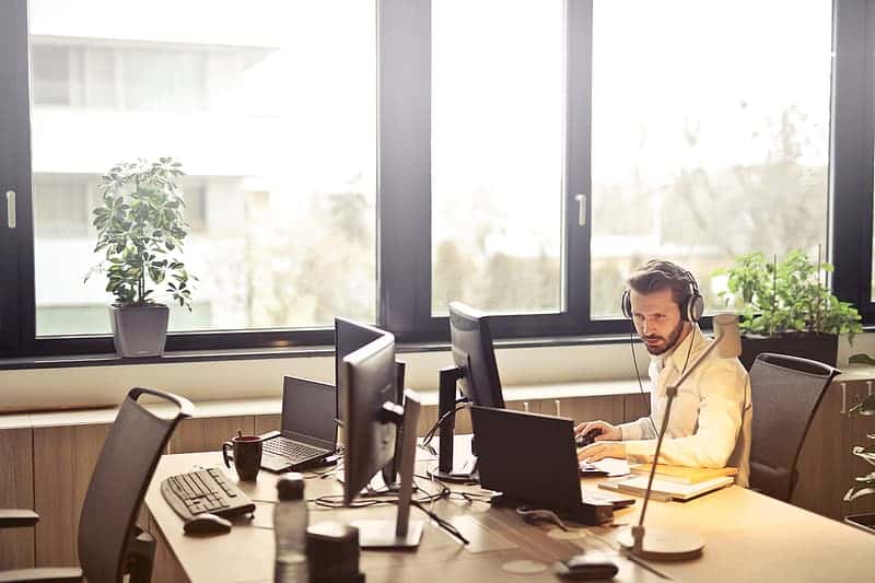 young-adult-man-in-white-shirt-working-at-computer-while-listening-music-with-headphones